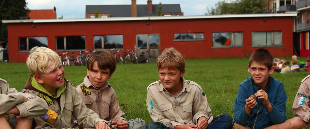 Welpen zitten voor het lokaal in kleermakerszit in het gras in een kring