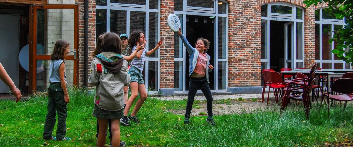 Leden spelen in het gras voor hun scoutslokaal