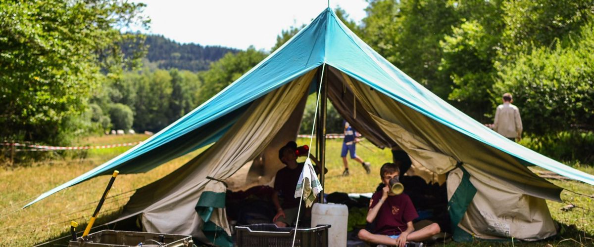 Een open staande patrouilletent. in de tent twee jongverkenners aan het uitrusten.